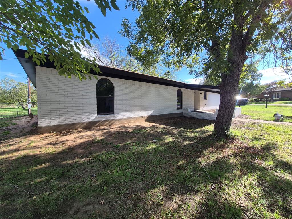 White painted brick exterior featuring arched window framing, a low-profile roofline, and mature trees on the grounds