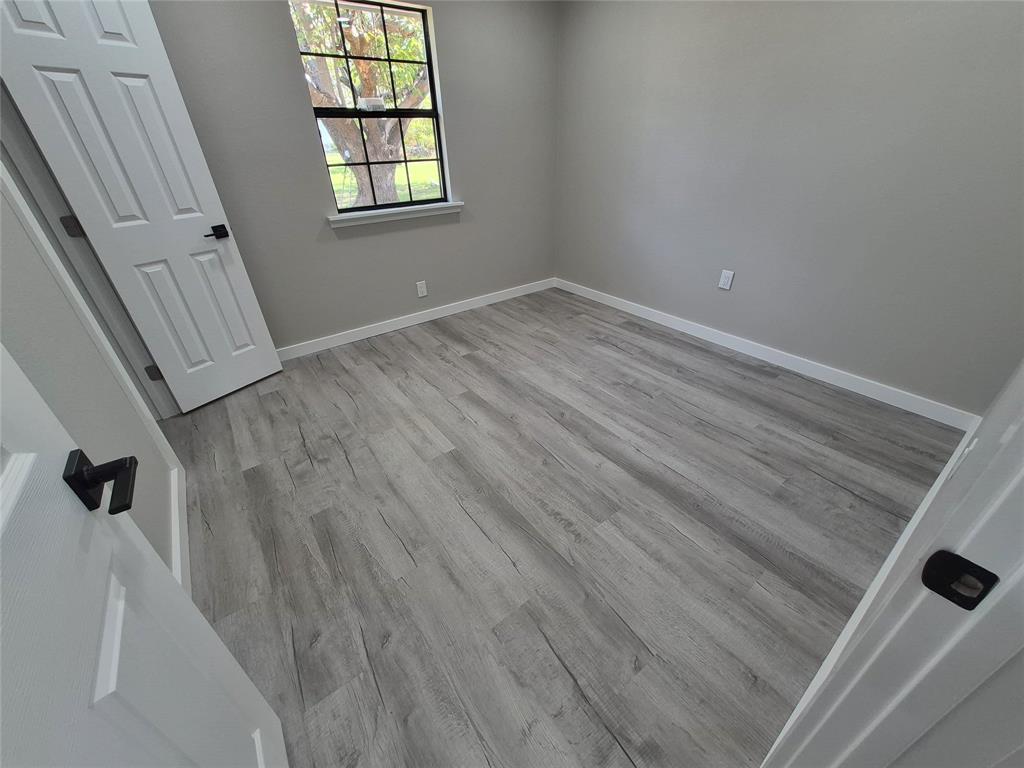 Room featuring wood-finish flooring, a single-hung window with a grid pattern, and interior doors with matte black hardware