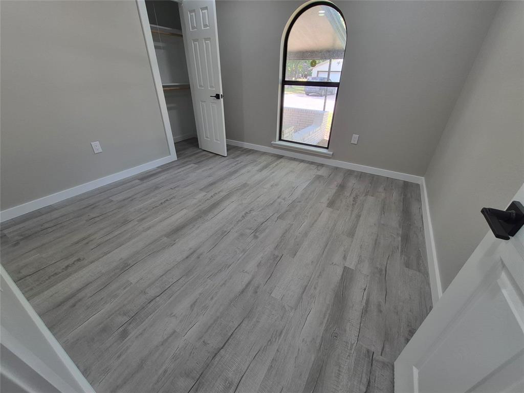 Room featuring wood-finish flooring, an arched window, and a built-in closet with six-panel door