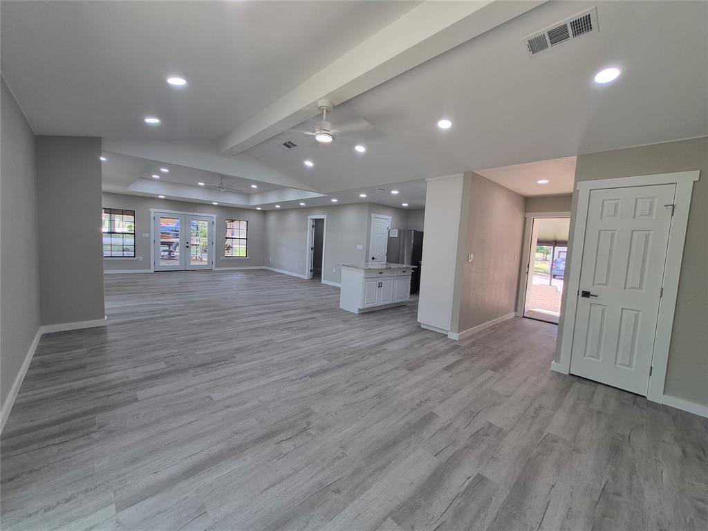 Open-concept interior featuring wood-finish flooring, recessed lighting, vaulted tray ceiling, and a central kitchen island with light-toned stone-finish countertop