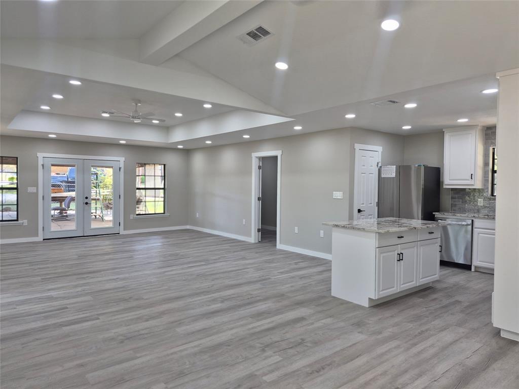 Open-concept interior featuring a vaulted tray ceiling, recessed lighting, wood-finish flooring, a kitchen island with stone countertops, and French doors