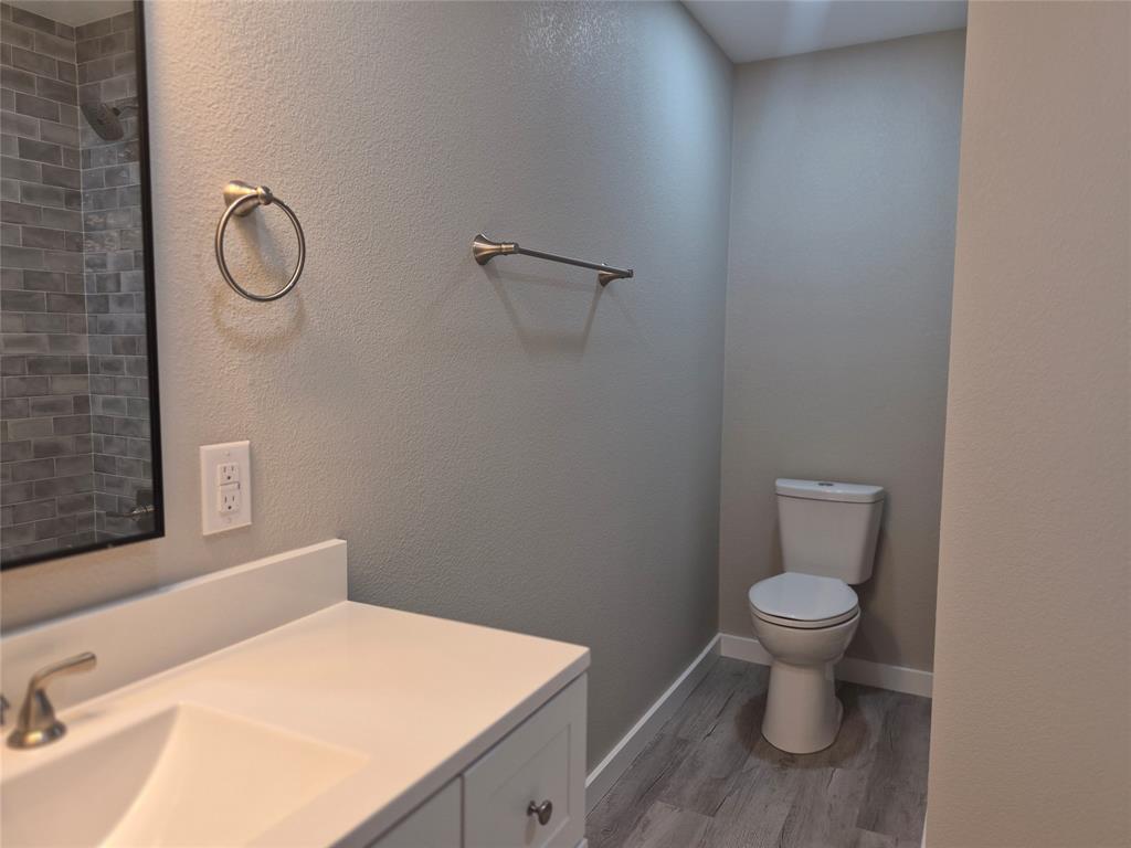 Bathroom featuring a white vanity with a solid-surface countertop, rectangular basin, wood-finish flooring, and subway tile shower surround