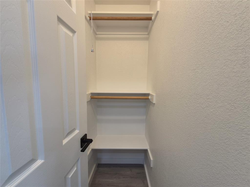 Storage space featuring dual-level shelving, integrated wood-finish garment rods, and a white six-panel door with matte black hardware