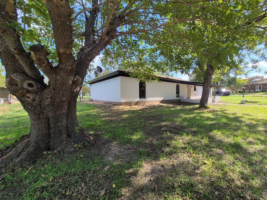 Single-story residence featuring white painted brick exterior, flat roofline, arched window detailing, and mature trees on a grass-covered lot