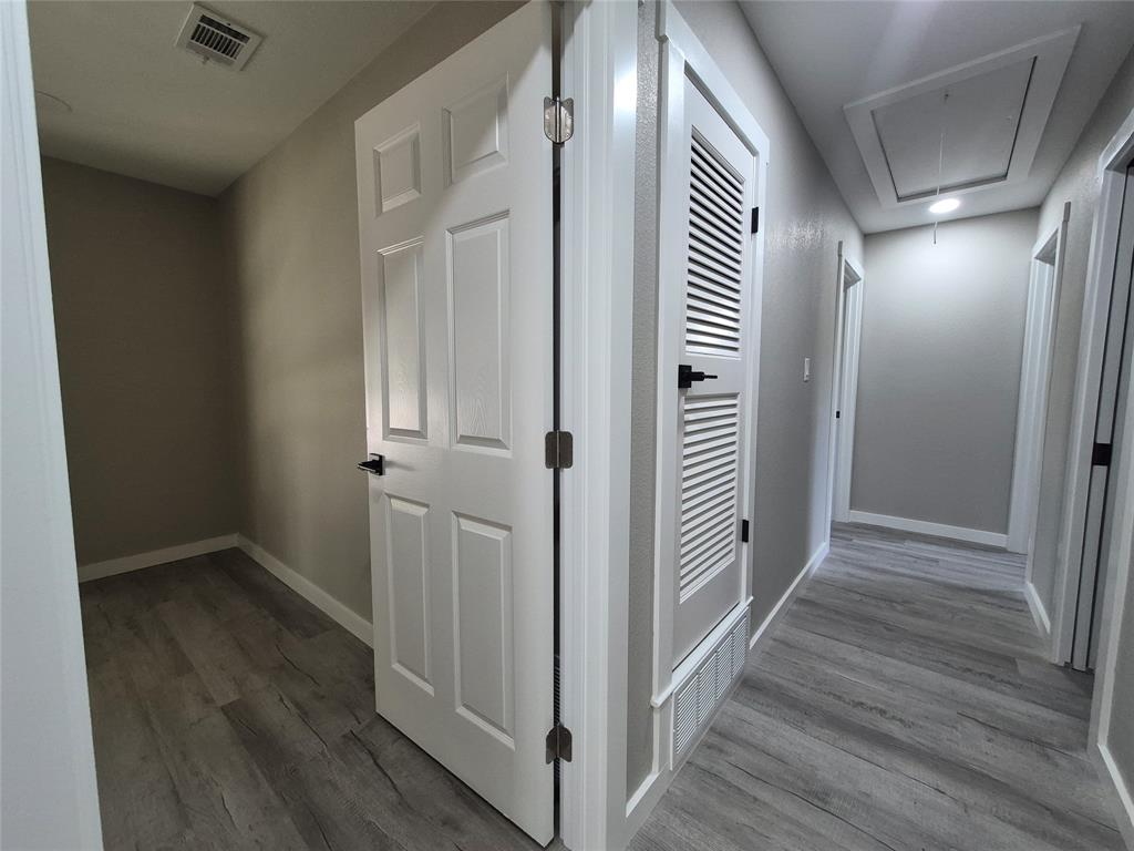 Hallway featuring wood-finish flooring, six-panel interior doors with matte black hardware, and an integrated louvered door utility closet