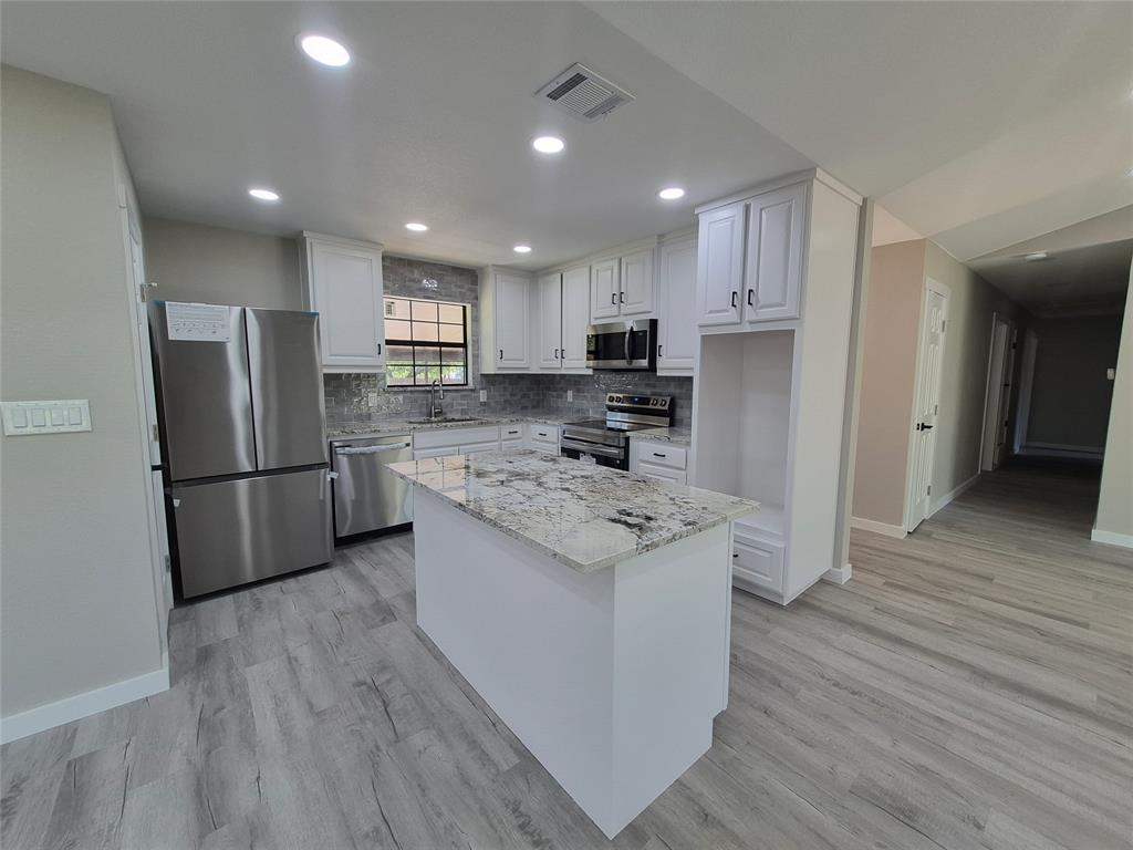Kitchen featuring white shaker-style cabinetry, stone-surface countertops, stainless steel appliances, a center island, and wood-finish flooring