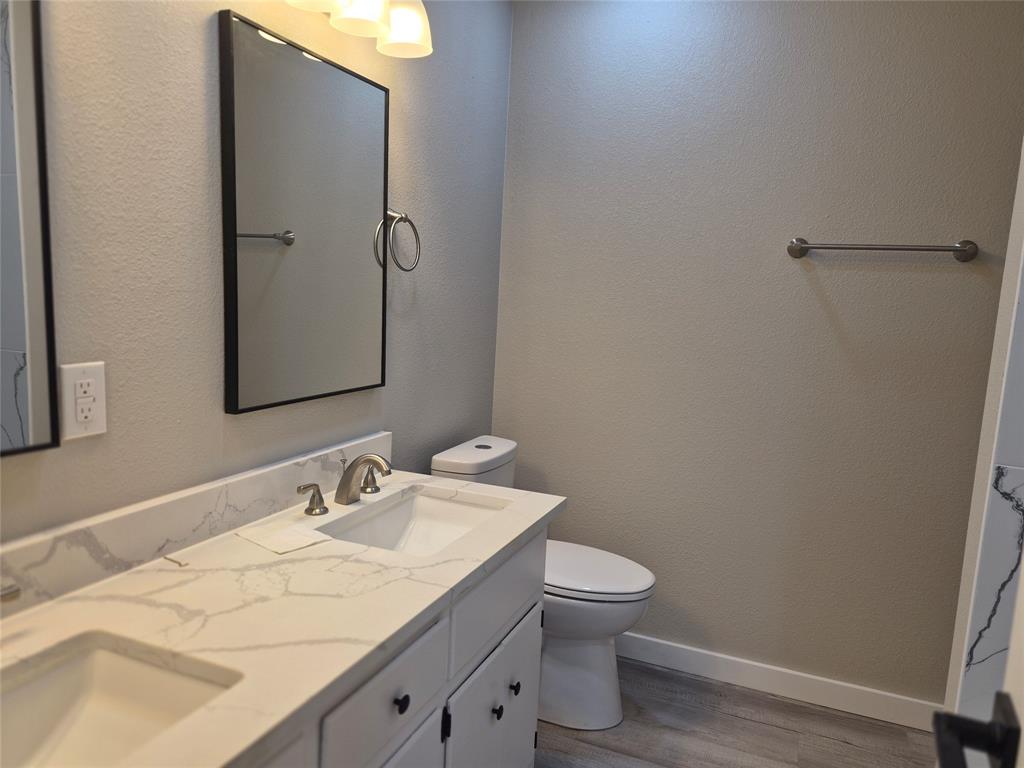 Double vanity featuring a light-toned stone-finish countertop with integrated dual sinks, sleek black hardware, framed wall mirrors, and wood-finish flooring
