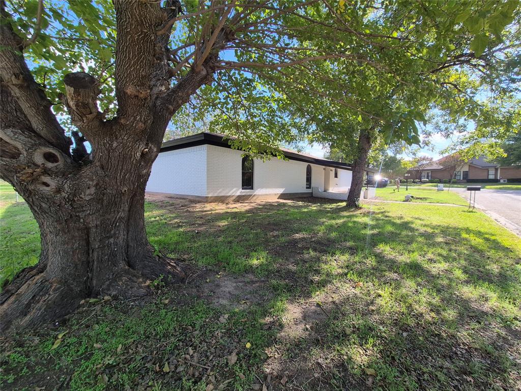 Single-story residence featuring a painted masonry exterior, arched window detailing, and mature shade trees