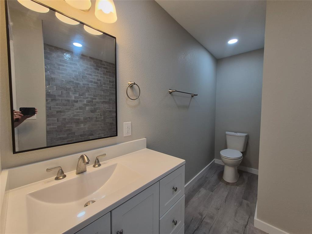 Vanity with a solid-surface countertop and integrated sink, rectangular mirror with a dark frame, metallic wall-mounted hardware, and wood-finish flooring