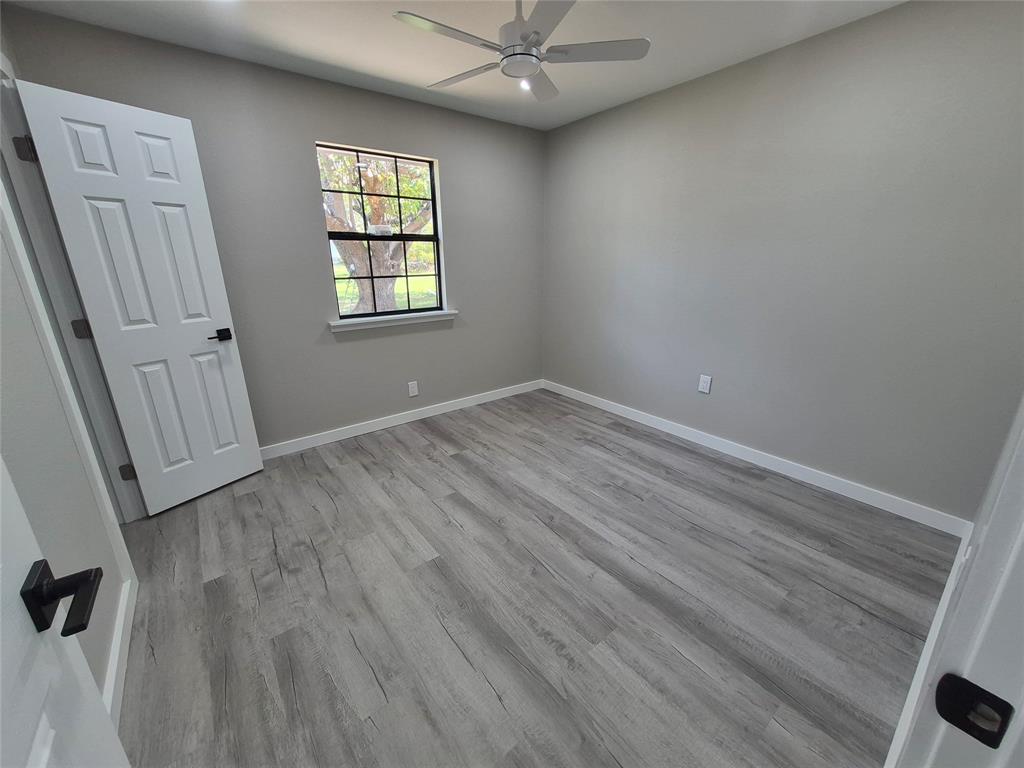 Room featuring wood-finish flooring, a multi-pane window, a ceiling fan, and six-panel interior doors with matte black hardware