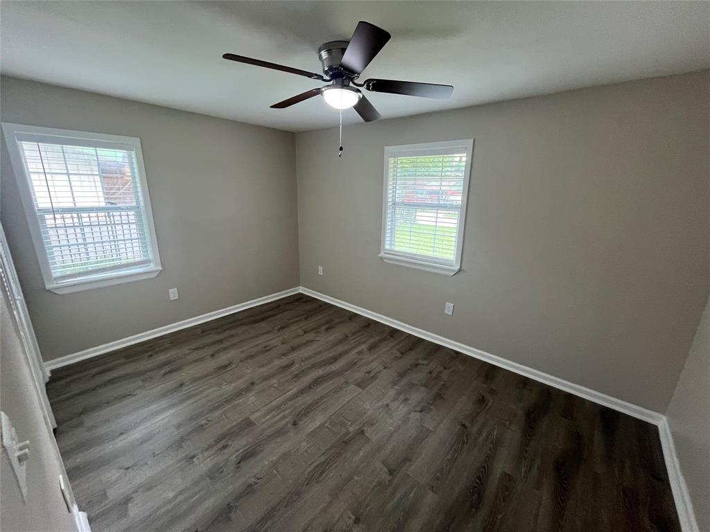 Room featuring neutral-toned walls, wood-finish flooring, two windows with horizontal blinds, and a central ceiling fan with an integrated light fixture