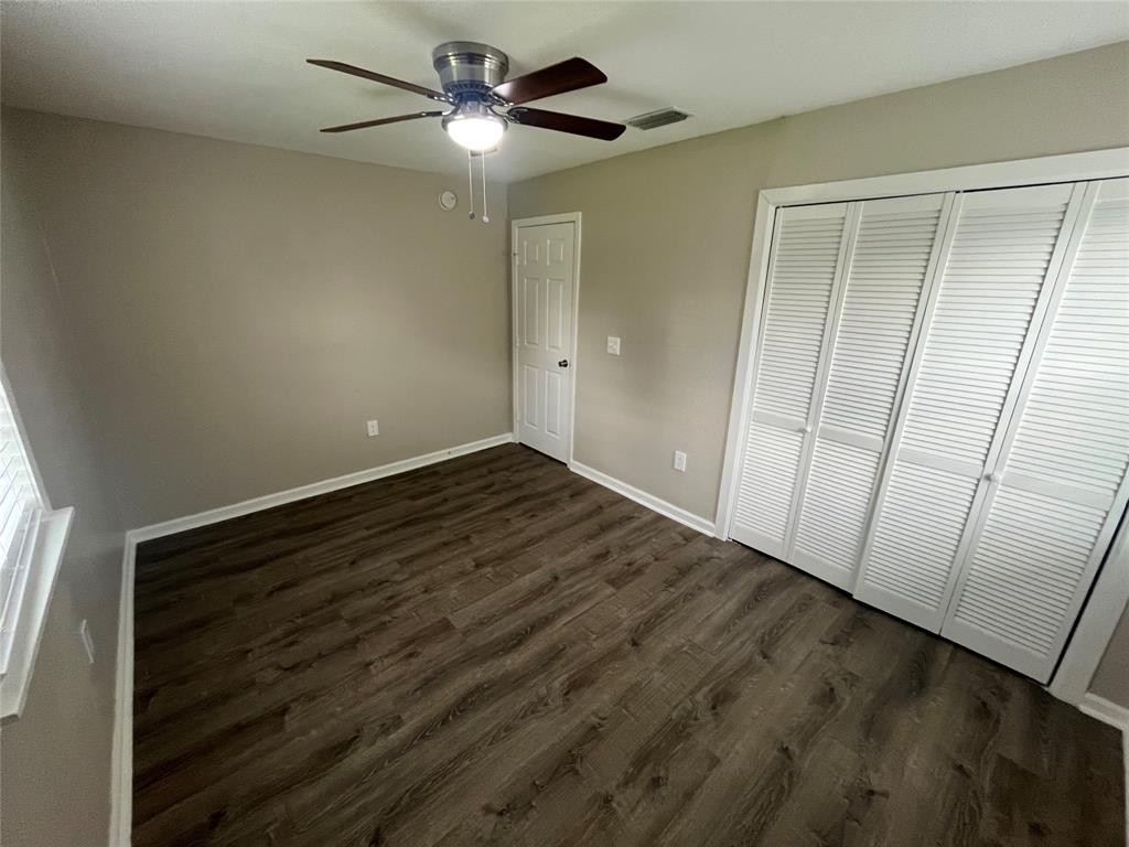Room featuring wood-finish flooring, a ceiling fan with integrated lighting, and a large closet with louvered double doors