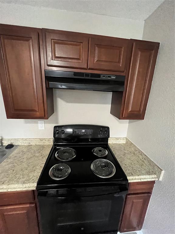 Stained wood cabinetry, black electric range with coil burners, over-the-range microwave, and stone-finish laminate countertops