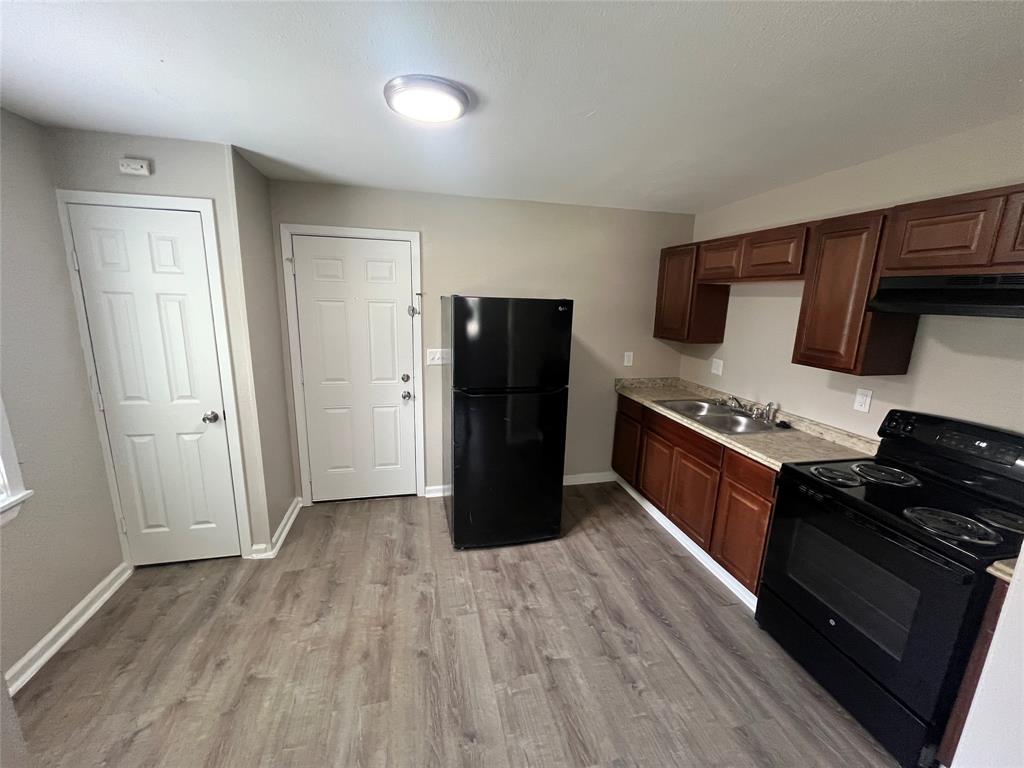 Kitchen featuring dark wood-finish cabinetry, solid-surface countertops, black finish appliances, and wood-finish flooring