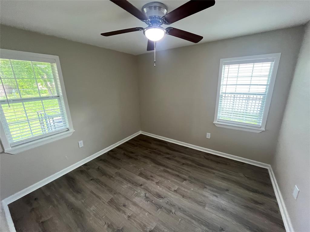 Neutral-toned interior space featuring wood-finish flooring, dual windows with horizontal blinds, and a central ceiling fan with integrated lighting