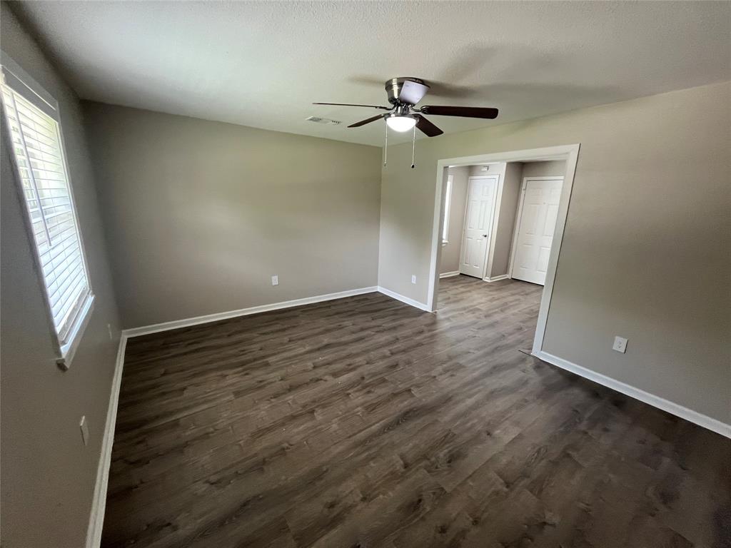 Wood-finish flooring, neutral wall tones, multi-blade ceiling fan with integrated lighting, and white six-panel interior doors