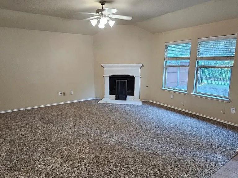 Vaulted ceilings, fireplace with a white mantel, neutral carpeting, and large windows with blinds