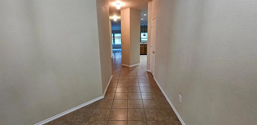 Interior hallway featuring large-format ceramic tile flooring, neutral wall paint, and overhead flush-mount lighting fixtures Interior hallway featuring large-format ceramic tile flooring, neutral wall paint, and overhead flush-mount lighting fixtures