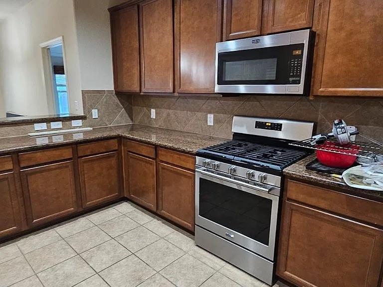 Kitchen featuring wood cabinetry, stone-finish countertops, ceramic tile backsplash, and stainless steel gas range with overhead microwave
