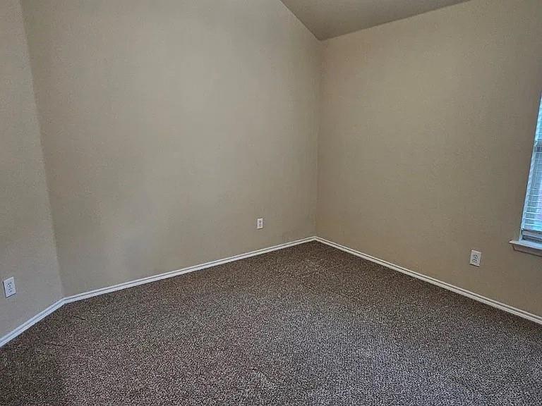 Neutral-toned interior space featuring vaulted ceilings, wall-to-wall carpeting, and a single window with blinds