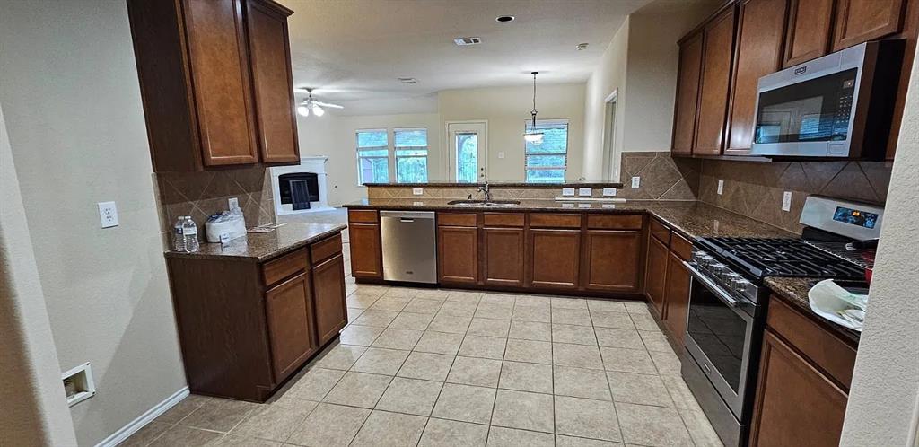 Kitchen featuring stained wood cabinetry, stone-surface countertops, tile backsplash, stainless steel appliances, and tile flooring