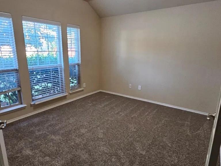 Interior space featuring a vaulted ceiling, neutral wall tones, wall-to-wall carpeting, and a trio of windows with horizontal blinds Interior space featuring a vaulted ceiling, neutral wall tones, wall-to-wall carpeting, and a trio of windows with horizontal blinds