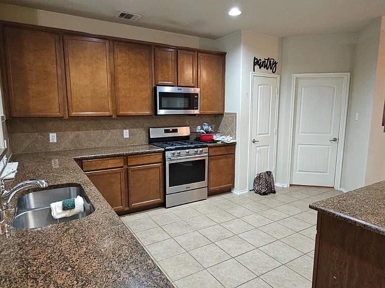 Kitchen featuring wood cabinetry, stone-surface countertops, tile backsplash, stainless steel appliances, and tile flooring