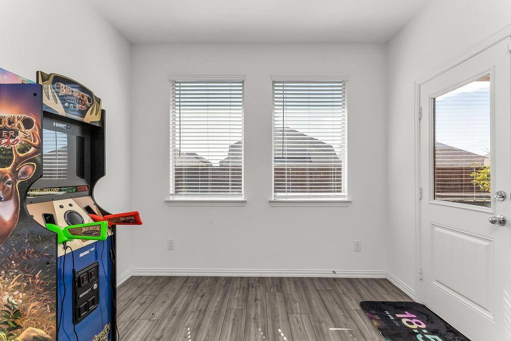 Neutral-toned room featuring vinyl flooring, dual windows with horizontal blinds, and a paneled exterior door with a glass insert