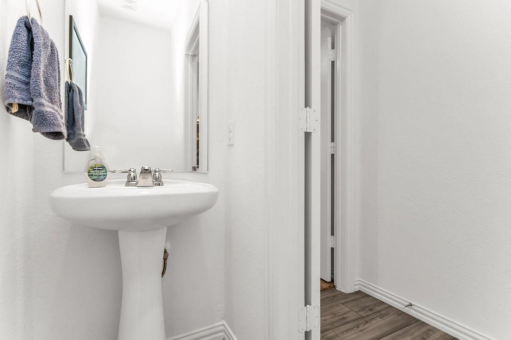 White pedestal sink with a polished chrome two-handle faucet, wall-mounted rectangular mirror, and dark-toned wood-finish flooring