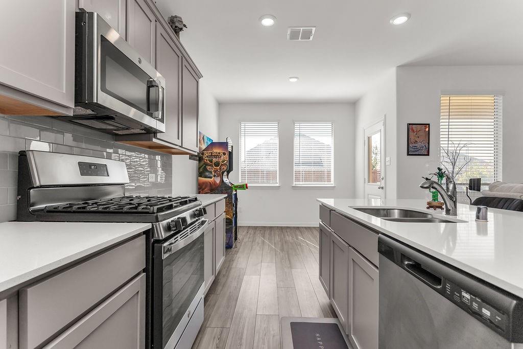 Kitchen featuring grey shaker-style cabinetry, quartz countertops, stainless steel appliances, grey subway tile backsplash, and vinyl flooring