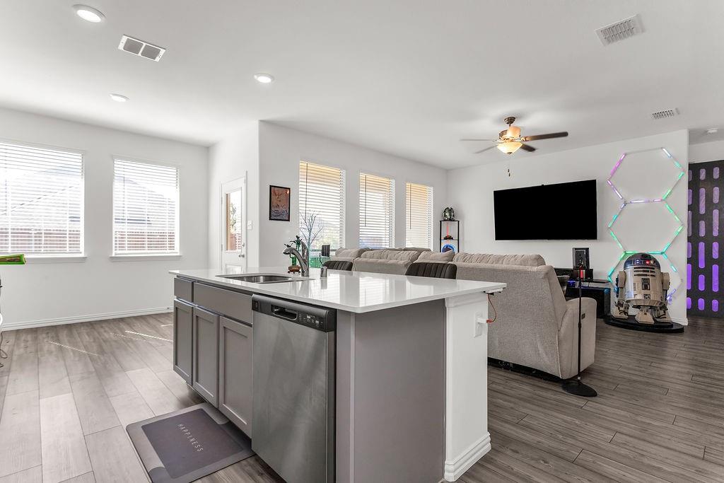 Kitchen island featuring a quartz countertop, stainless steel dishwasher, and undermount sink, complemented by vinyl flooring and recessed lighting
