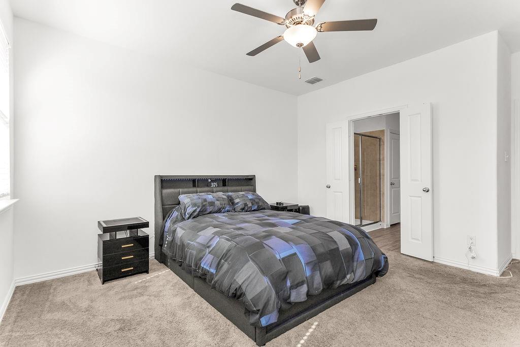 Neutral-toned carpeting, ceiling fan with integrated light fixture, and interior doors opening to tiled bathroom