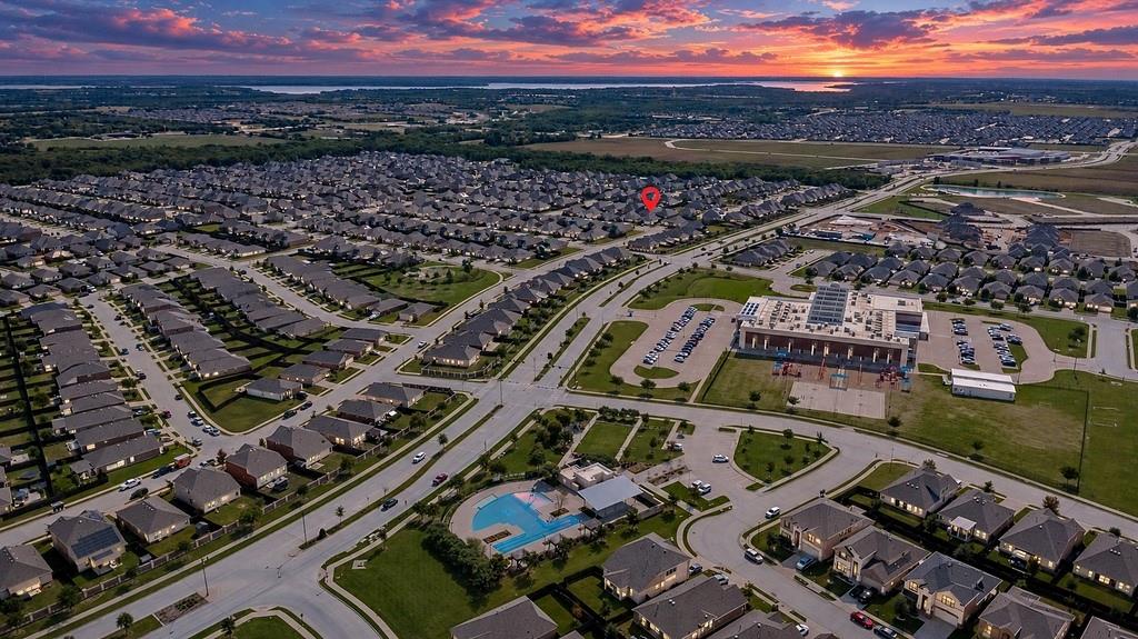 Aerial perspective of a master-planned community featuring proximity to a neighborhood swimming pool, recreational facilities, and expansive open space under a sunset horizon