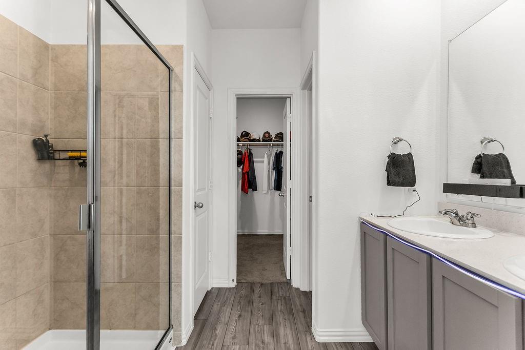 Walk-in shower with tile surround and glass door, gray cabinetry, integrated sink, and wood-finish flooring