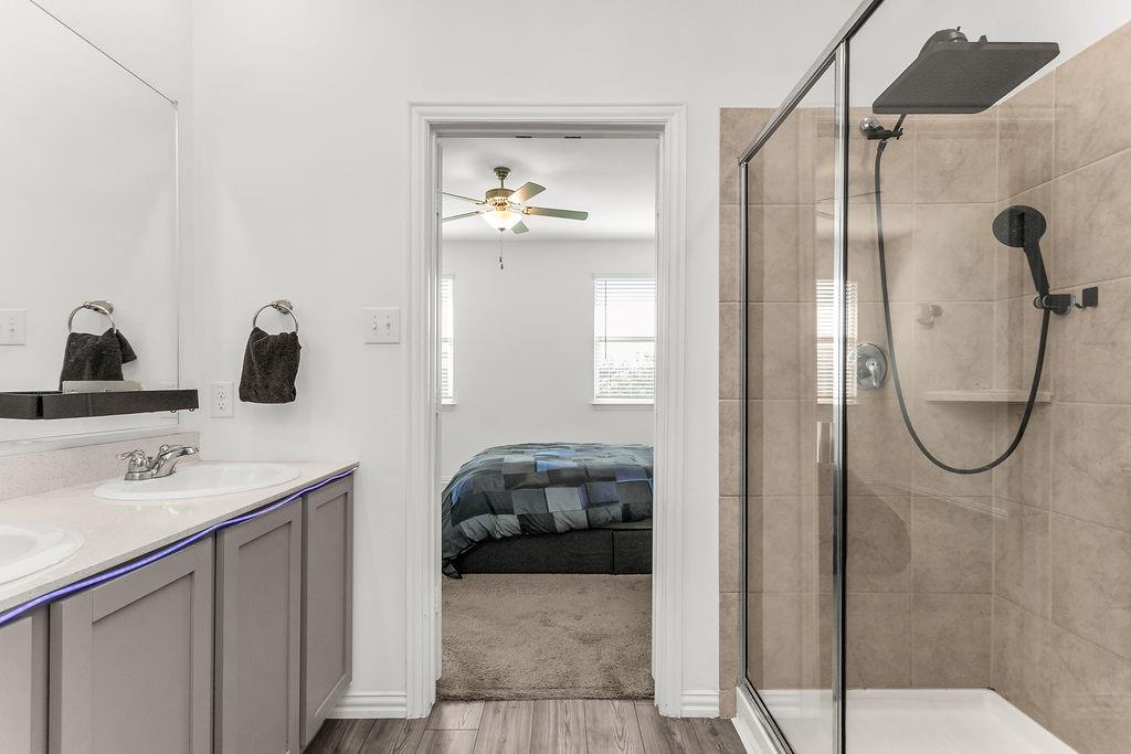Dual-sink vanity with light-toned countertop, framed glass-enclosed shower featuring tile surround, and rainfall shower head with handheld attachment
