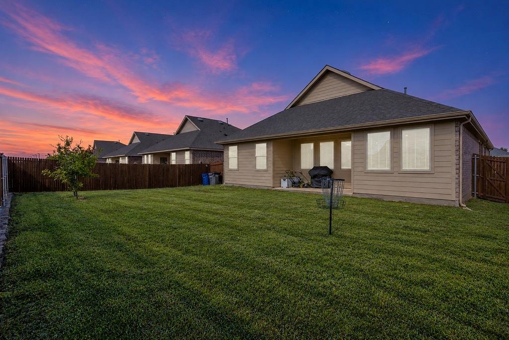 Backyard featuring a concrete patio, sodded lawn, and perimeter wood fencing under a colorful sky