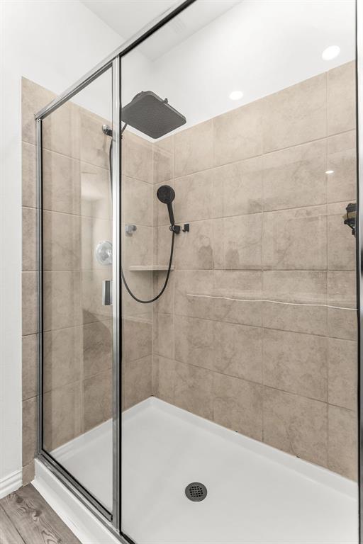 Walk-in shower featuring glass paneling, floor-to-ceiling tile surround, square rainfall shower head, handheld sprayer, and integrated corner shelving