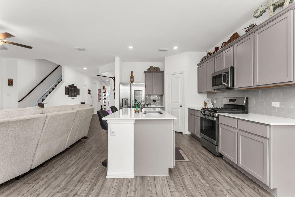 Kitchen featuring gray cabinetry, a central island with a white countertop, stainless steel appliances, and vinyl flooring