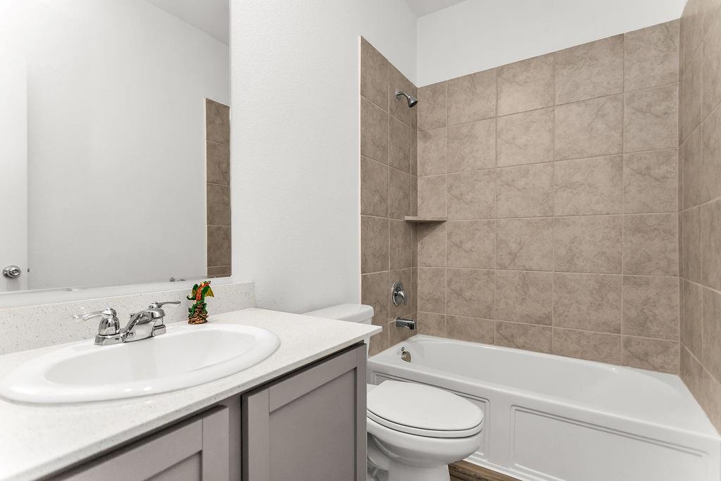 Bathroom featuring a vanity with a light-toned solid surface countertop, inset sink, chrome fixtures, and a tub-shower combination with floor-to-ceiling neutral tile surround