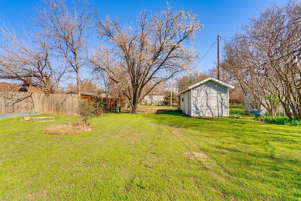 Expansive backyard featuring a mature canopy tree, wood perimeter fencing, and a detached structure with siding