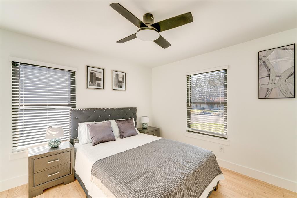 Neutral-toned interior featuring wood-finish flooring, two windows with horizontal blinds, and a ceiling fan with integrated lighting