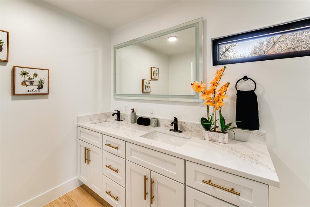 Double vanity featuring white cabinetry, stone-patterned countertops with dual integrated sinks, matte black widespread faucets, metallic hardware, and a large rectangular mirror