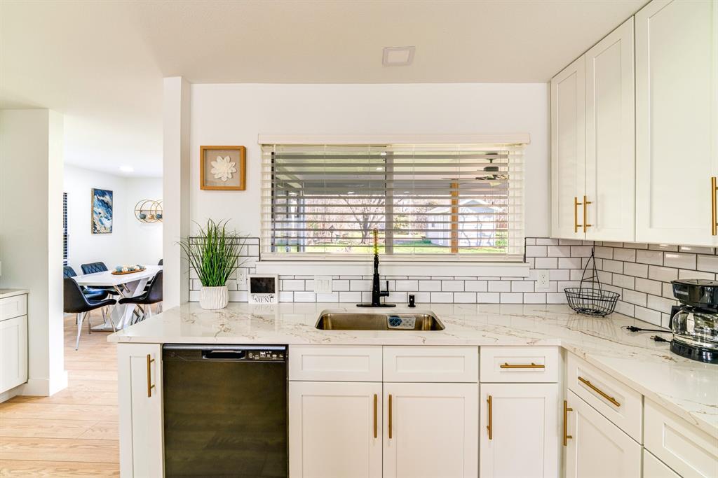 Kitchen featuring white Shaker-style cabinetry, gold-tone hardware, white subway tile backsplash, stone-finish countertops, and a single-basin undermount sink with a matte black faucet Kitchen featuring white Shaker-style cabinetry, gold-tone hardware, white subway tile backsplash, stone-finish countertops, and a single-basin undermount sink with a matte black faucet