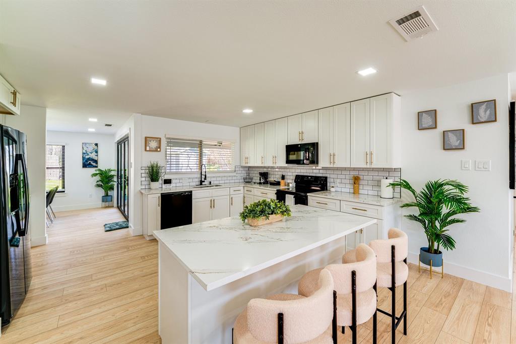 Kitchen featuring white cabinetry with gold-toned hardware, a quartz-surfaced island, subway tile backsplash, and light-toned wood-finish flooring Kitchen featuring white cabinetry with gold-toned hardware, a quartz-surfaced island, subway tile backsplash, and light-toned wood-finish flooring