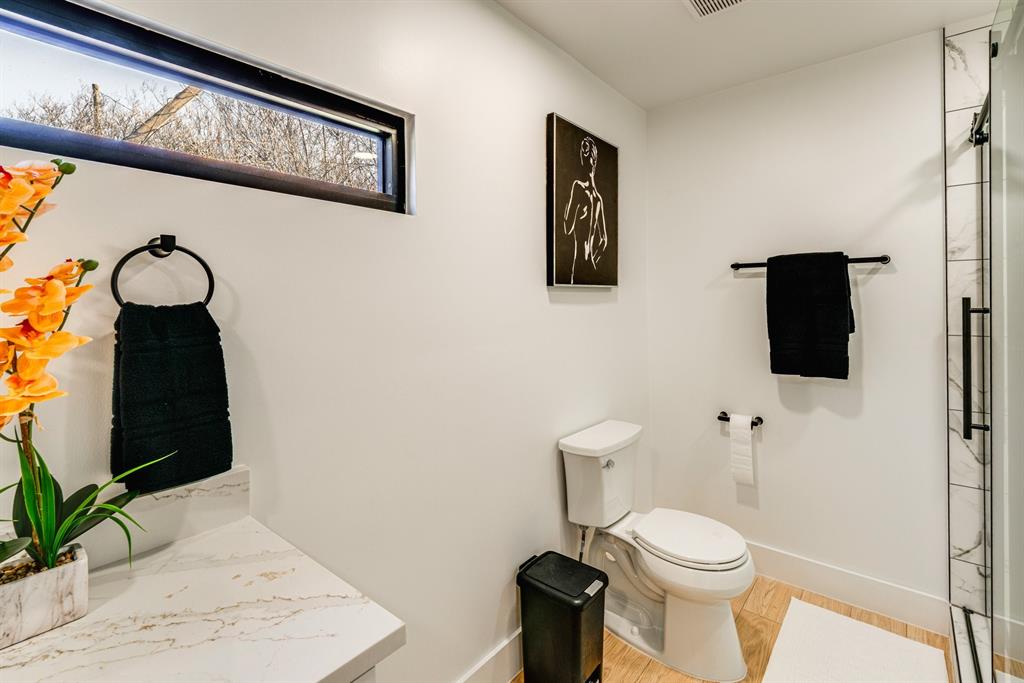 Bathroom featuring a horizontal clerestory window, stone-finish vanity countertop, wood-finish flooring, and a walk-in shower with tiled surround