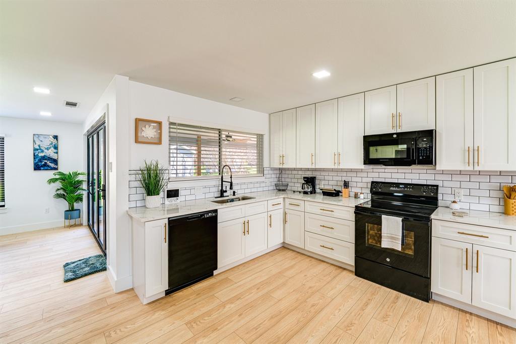 Kitchen featuring white shaker-style cabinetry with gold-toned hardware, stone-surface countertops, subway tile backsplash, and black appliances including a built-in microwave