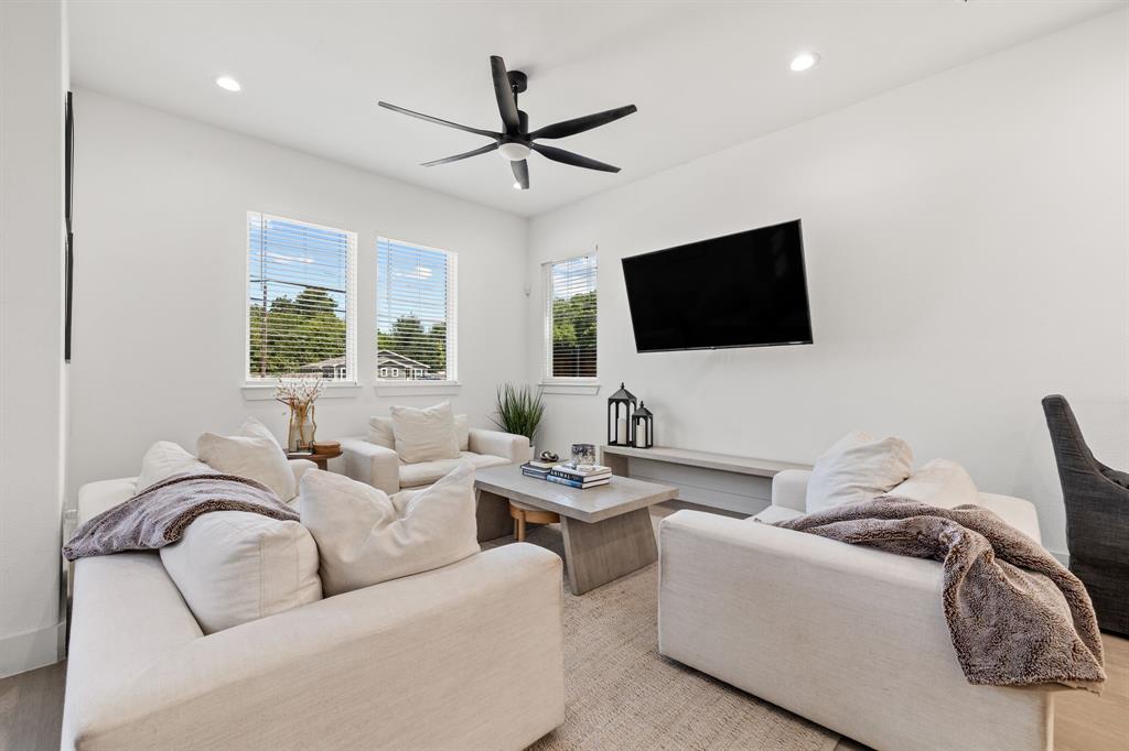 Living area featuring high ceilings, recessed lighting, a multi-blade ceiling fan, three windows with horizontal blinds, and a built-in floating shelf Living area featuring high ceilings, recessed lighting, a multi-blade ceiling fan, three windows with horizontal blinds, and a built-in floating shelf