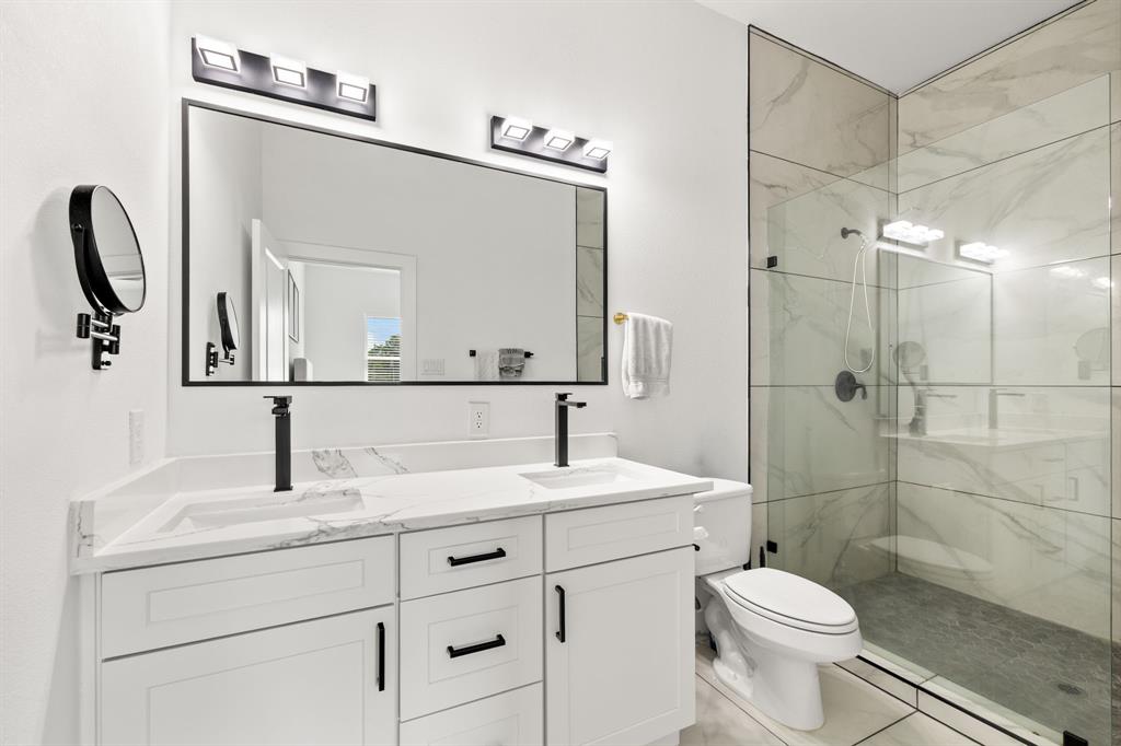 Dual-sink vanity with white cabinetry, stone-finish countertop, and matte black fixtures, paired with a glass-enclosed shower featuring large-format tile surround and matte black hardware