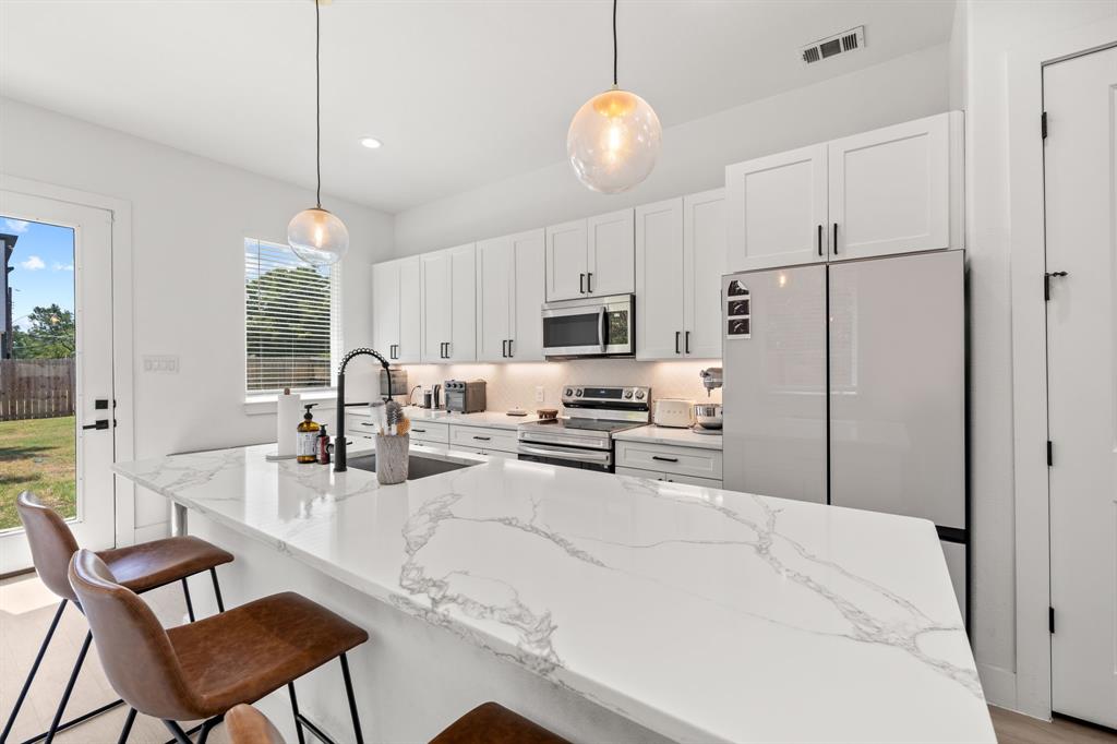 Kitchen featuring white cabinetry, quartz countertops with veining, stainless steel appliances, matte black hardware, and pendant lighting Kitchen featuring white cabinetry, quartz countertops with veining, stainless steel appliances, matte black hardware, and pendant lighting