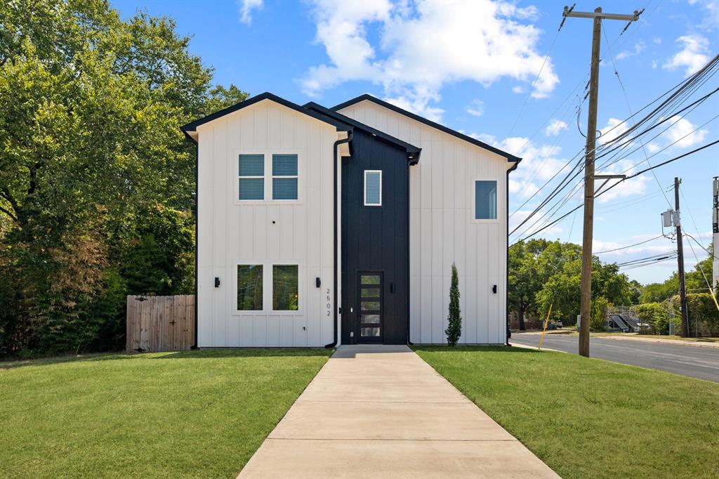 Two-story exterior featuring vertical white panel siding with black accent trim, a central entryway with a glass-paneled door, and a concrete walkway